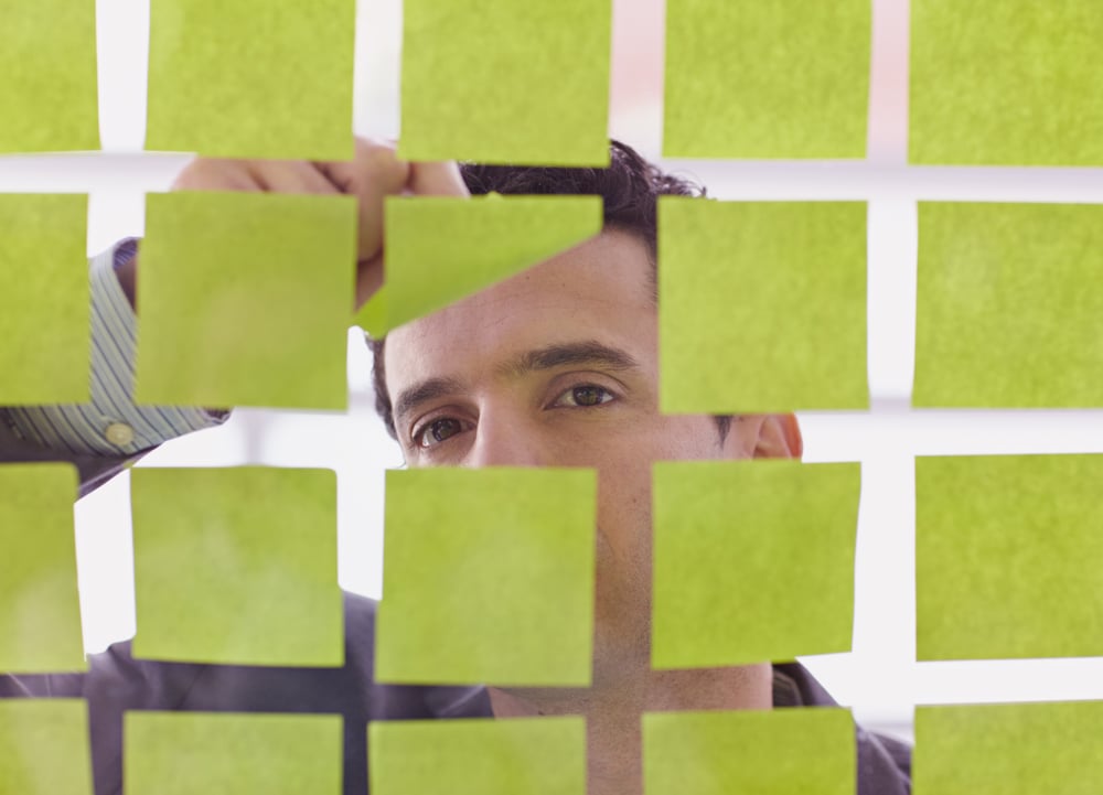 Portrait of a middle eastern business man behind sticky notes in bright glass office-1 Portrait of a middle eastern business man behind sticky notes in bright glass office-1